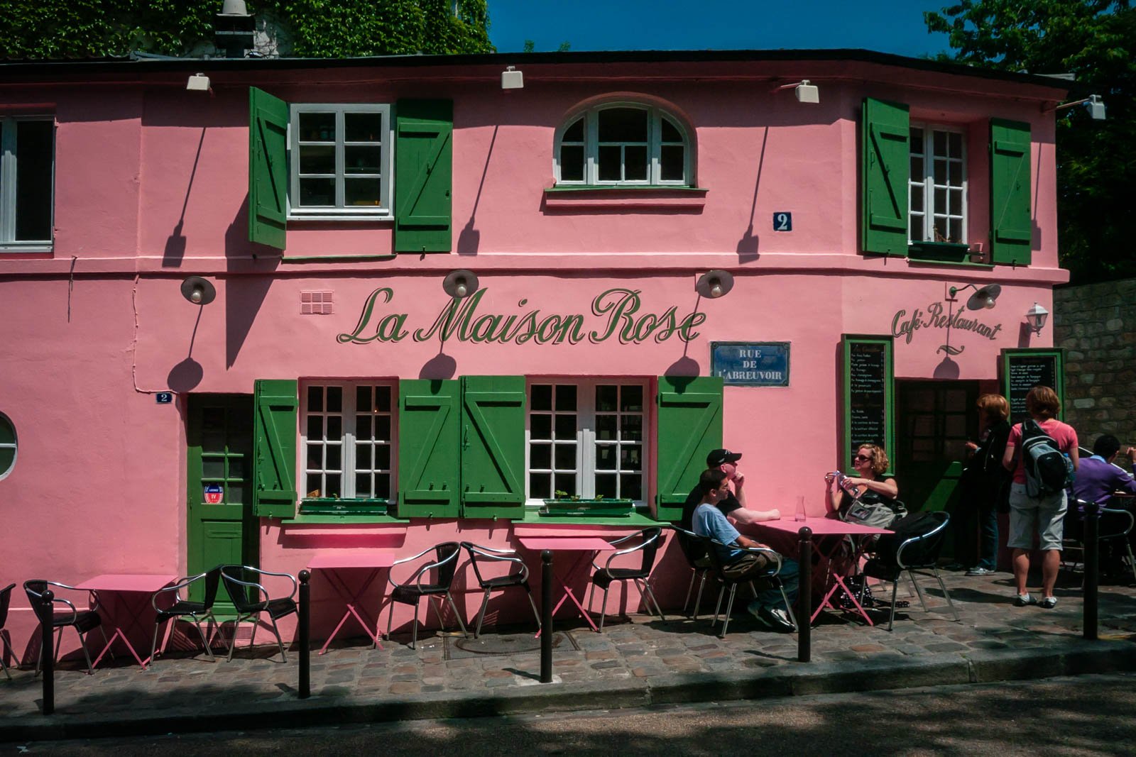 A vibrant, cobblestoned street in the Montmartre neighbourhood of Paris, with people sitting in the cafe.