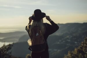 Woman wearing a hat and backpack looking out at a view of mountains