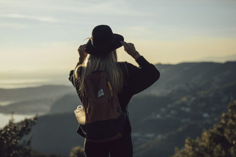 Woman wearing a hat and backpack looking out at a view of mountains